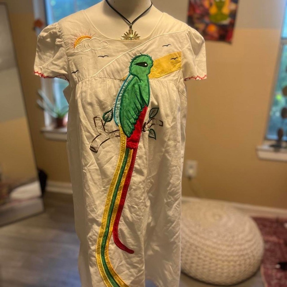 White babydoll dress with green bird graphic with red/yellow tail feathers